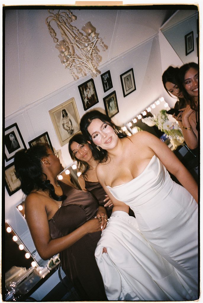 Bride laughing with her bridesmaids in the getting-ready room mirror, on film
