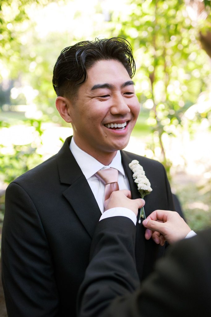 Groom laughing as his boutonniere is pinned