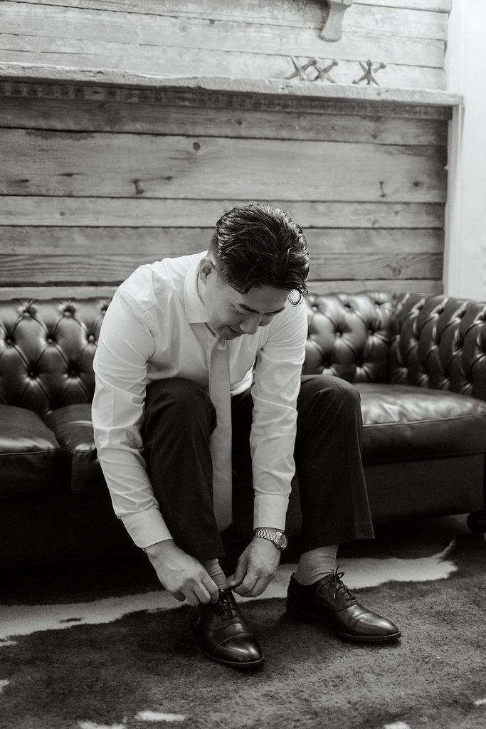 Groom tying his shoes on a leather sofa, black and white