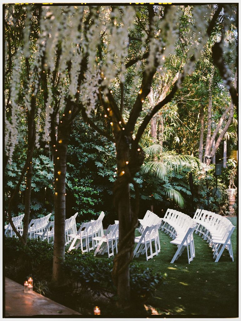 Empty white ceremony chairs under hanging blooms at Hartley Botanica, on film