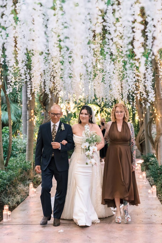 Bride and her parents on the aisle beneath hanging flowers
