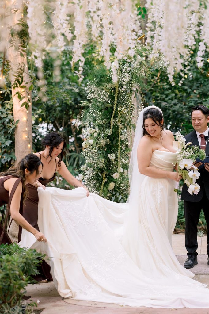 Bridesmaid adjusting the bride's train on the ceremony aisle
