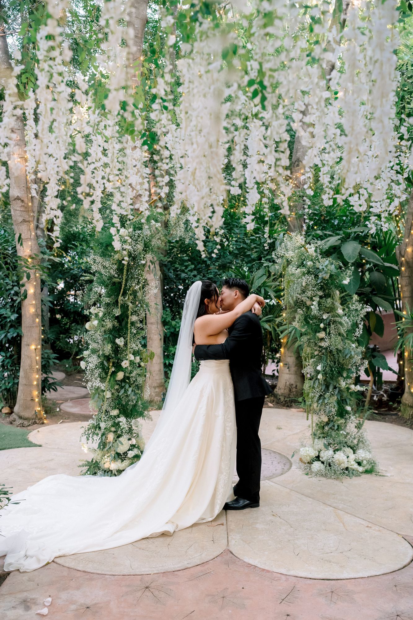 bride and groom sharing their first kiss at their hartley botanica wedding under wisteria and in front of a green and white wedding arch