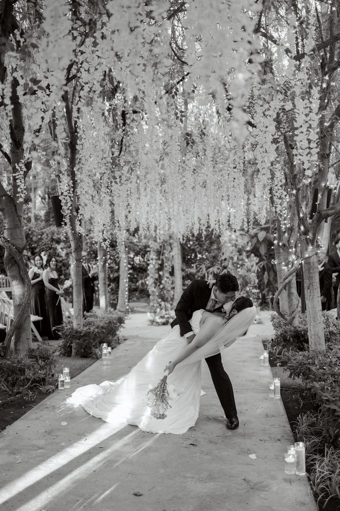 Newlyweds walking back up the aisle beneath white blooms, black and white