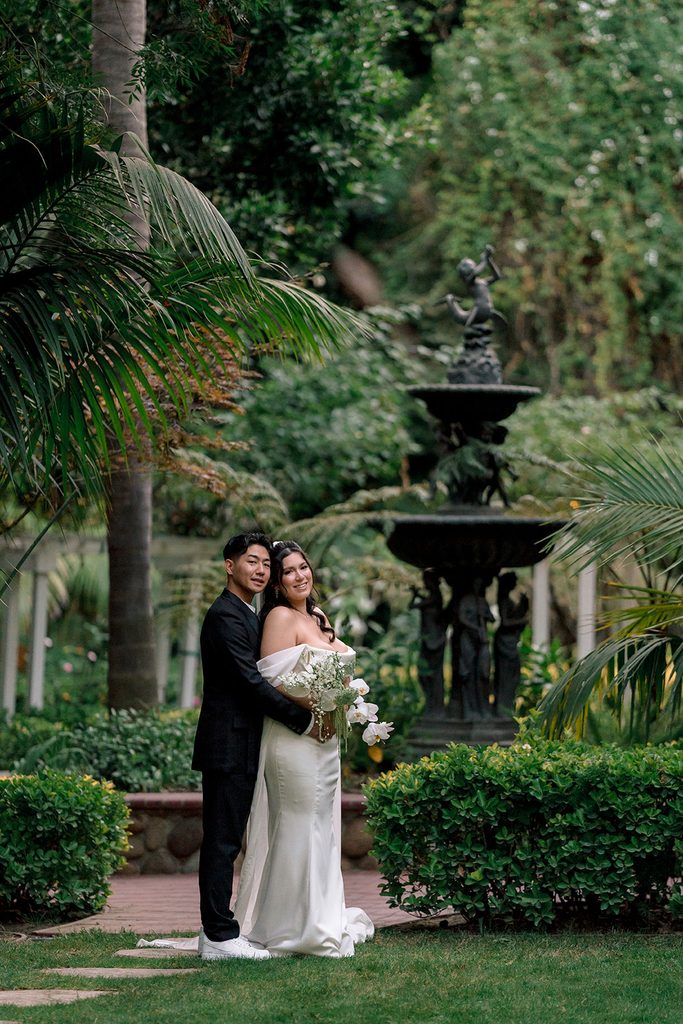 Bride and groom at the stone fountain at Hartley Botanica