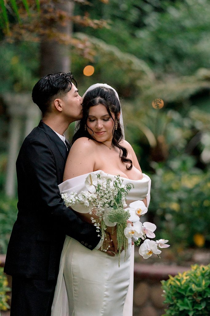Groom kissing the bride's forehead beside the fountain