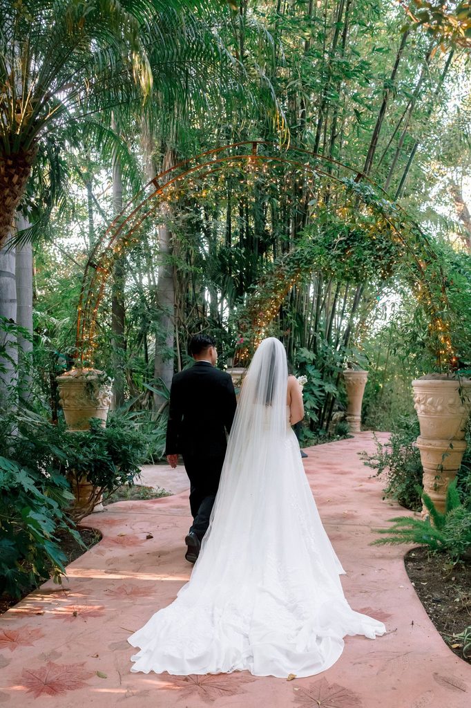 Bride and groom walking the brick garden path at Hartley Botanica with her veil trailing