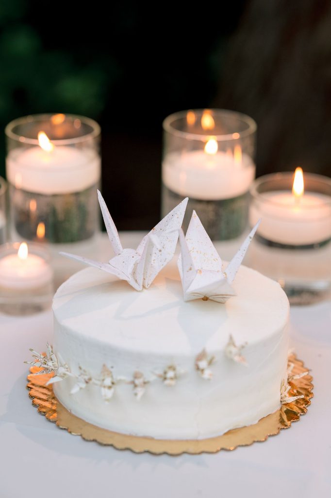 White wedding cake topped with paper cranes beside candles
