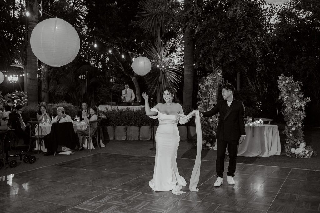 Newlyweds on the dance floor beneath paper lanterns, black and white