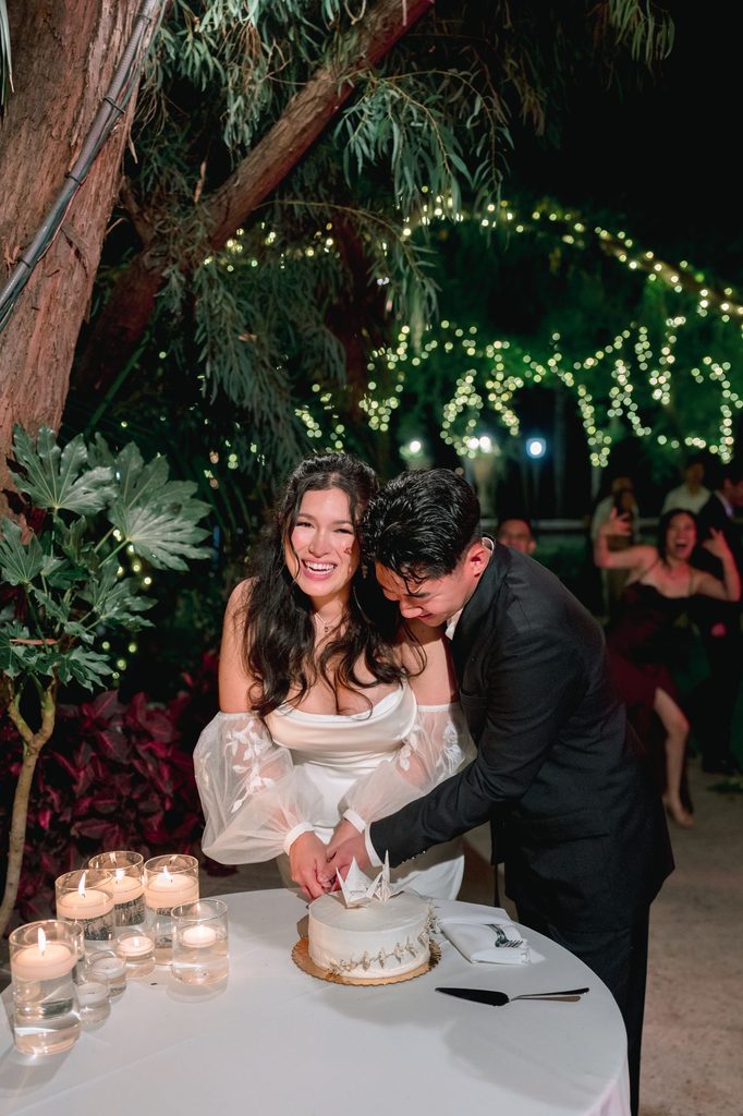 Bride and groom cutting the cake under string lights